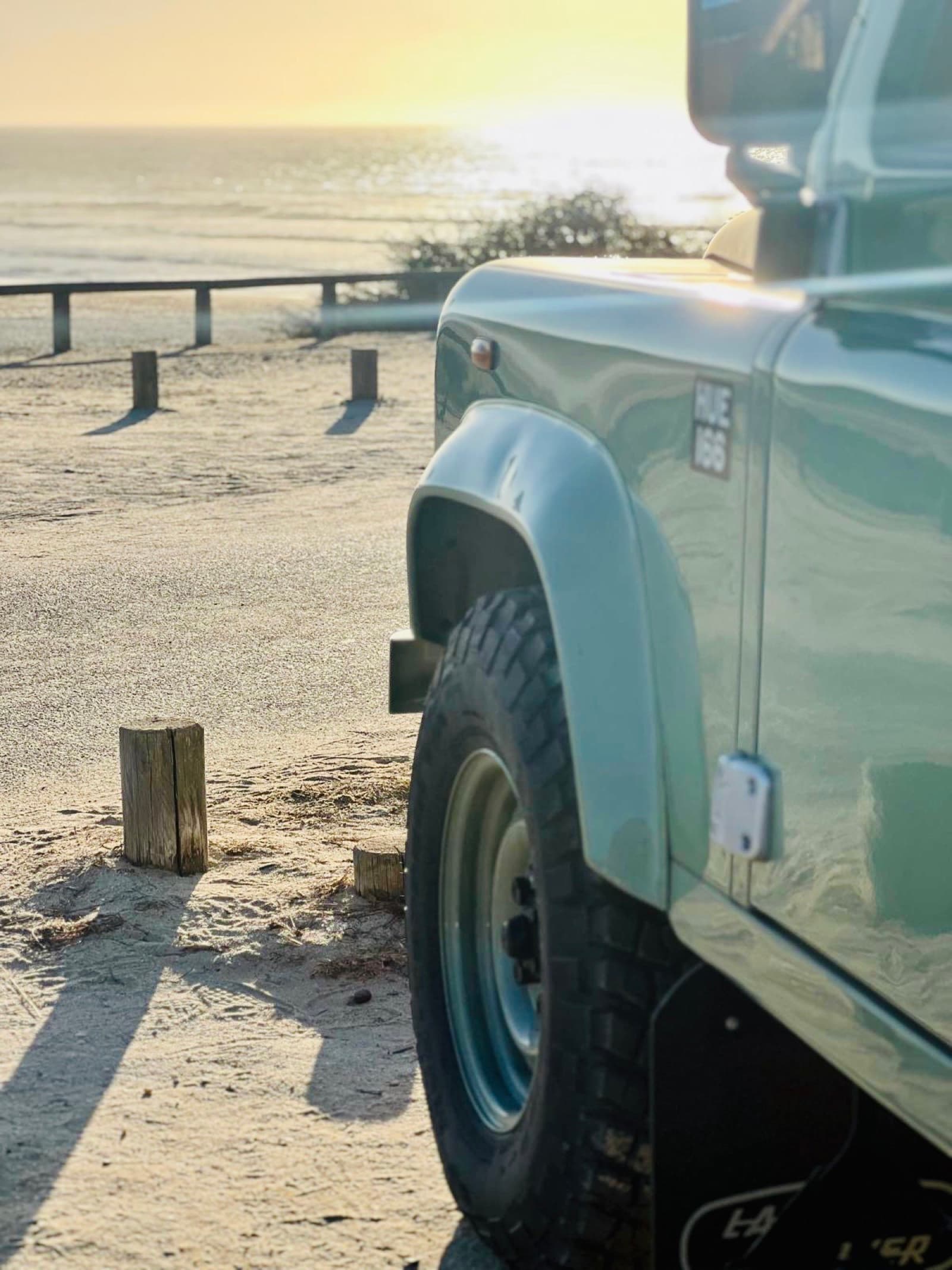 Land Rover Defender Heritage in Grasmere Green, parked at the beach at golden hour