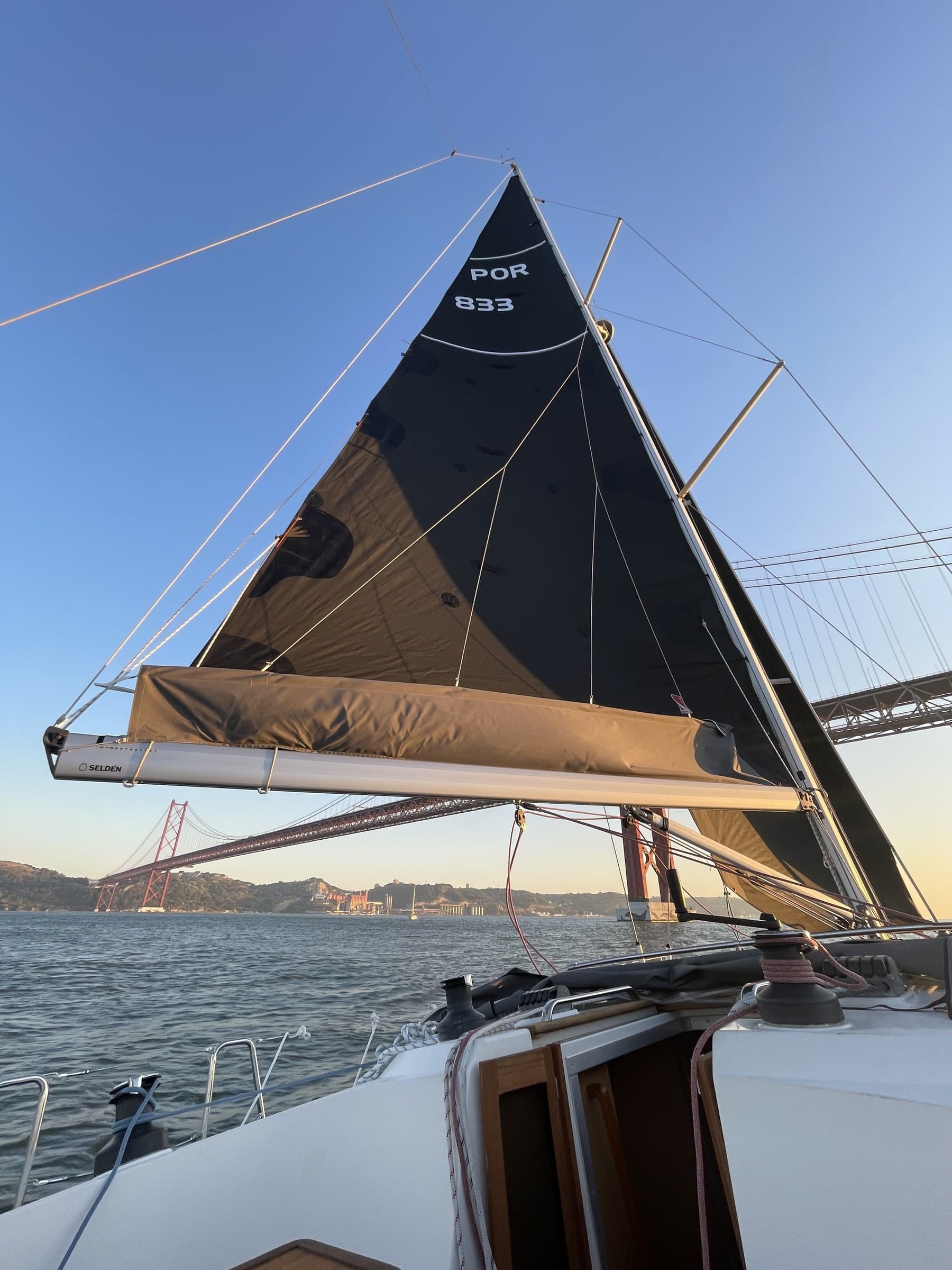 Mainsail of the Bavaria 42 framing the 25 de Abril bridge at golden hour